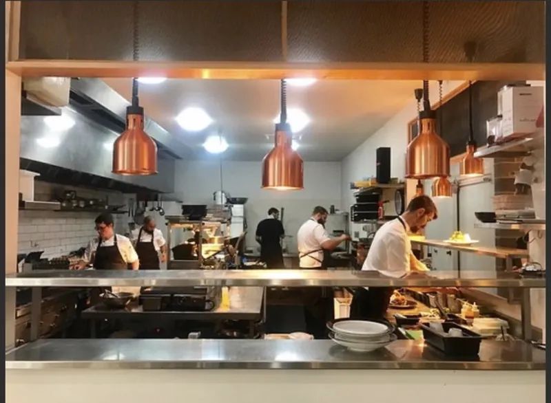 Chefs at work in the open kitchen under copper pendant lamps